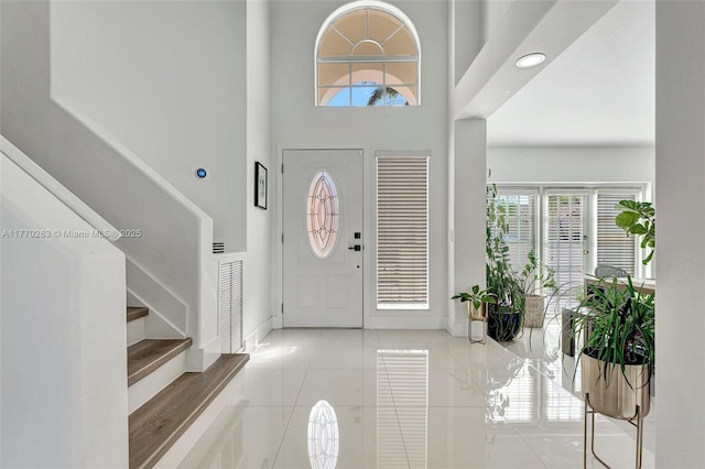 tiled entrance foyer featuring baseboards, plenty of natural light, stairs, and visible vents