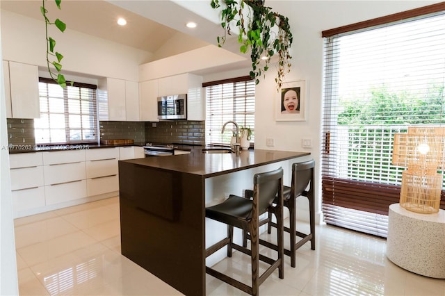 kitchen with appliances with stainless steel finishes, modern cabinets, dark countertops, a sink, and a peninsula
