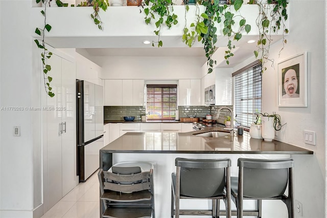 kitchen with a healthy amount of sunlight, a sink, freestanding refrigerator, stainless steel microwave, and a peninsula
