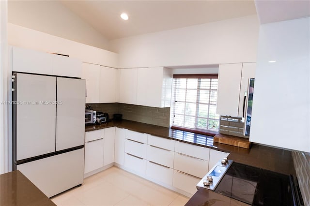kitchen featuring freestanding refrigerator, backsplash, dark countertops, and white cabinets