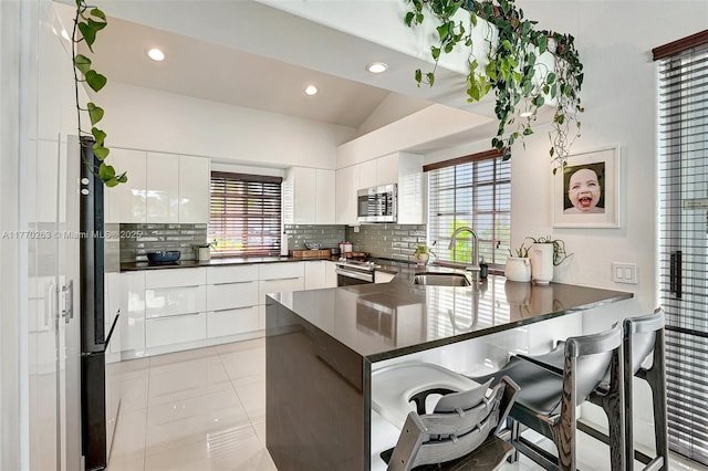 kitchen featuring appliances with stainless steel finishes, modern cabinets, dark countertops, a sink, and a peninsula