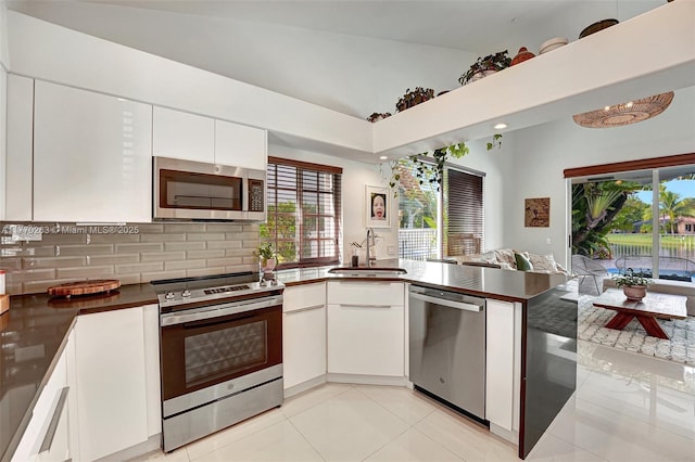 kitchen featuring dark countertops, appliances with stainless steel finishes, a sink, a peninsula, and backsplash