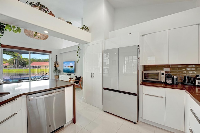 kitchen featuring stainless steel dishwasher, freestanding refrigerator, a toaster, dark countertops, and light tile patterned floors