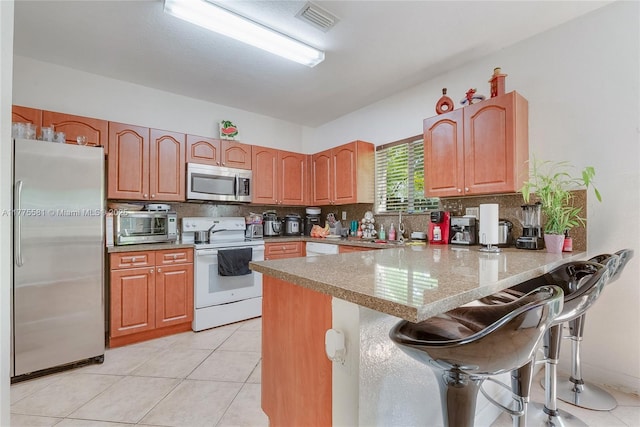 kitchen featuring stainless steel appliances, visible vents, a peninsula, a kitchen bar, and tasteful backsplash