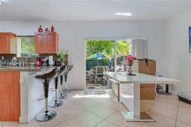 kitchen featuring light tile patterned flooring, decorative backsplash, brown cabinets, and a breakfast bar area