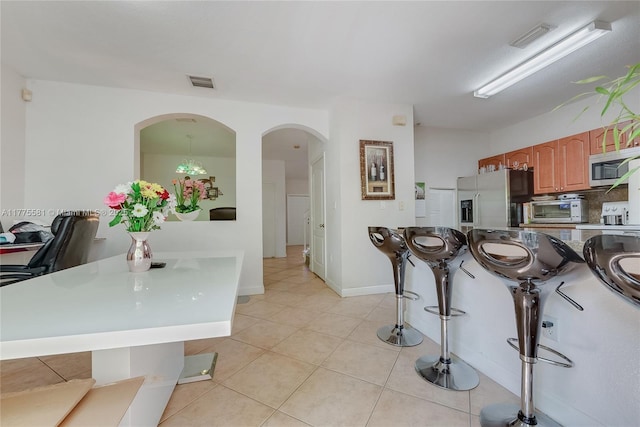 kitchen with a kitchen breakfast bar, light tile patterned floors, arched walkways, appliances with stainless steel finishes, and visible vents