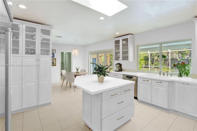 kitchen featuring stainless steel dishwasher, a center island, a sink, light tile patterned floors, and light countertops