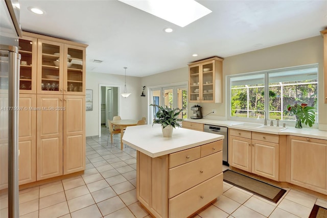 kitchen featuring light brown cabinetry, light countertops, dishwasher, a sink, and a kitchen island
