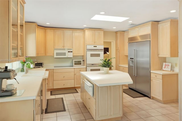 kitchen featuring white appliances, a sink, light brown cabinetry, and a warming drawer