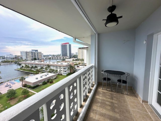 balcony with ceiling fan, a water view, and a view of city