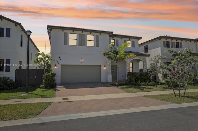 view of front facade with stucco siding, a tile roof, decorative driveway, and a garage