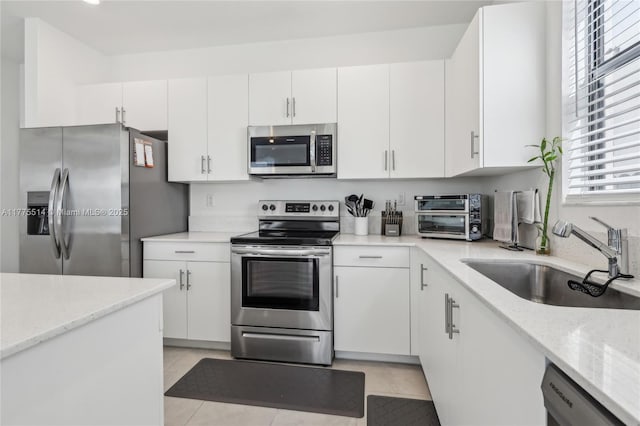 kitchen with stainless steel appliances, a toaster, a sink, white cabinetry, and light stone counters
