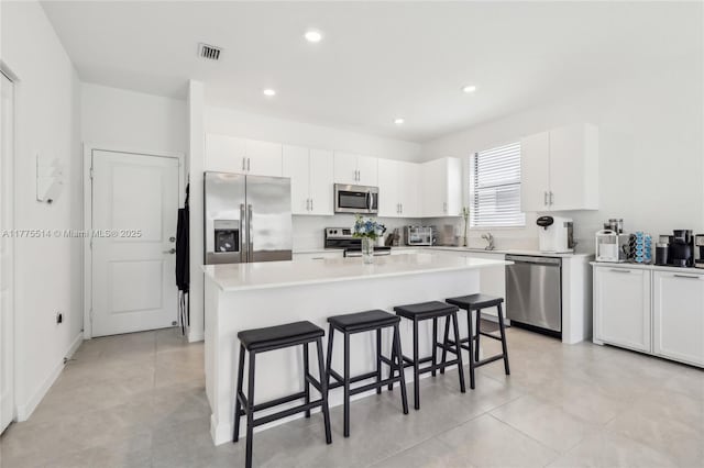kitchen featuring a breakfast bar area, white cabinets, appliances with stainless steel finishes, visible vents, and a kitchen island