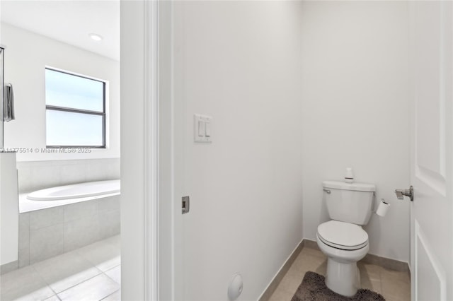 bathroom with tile patterned floors, baseboards, toilet, and tiled tub