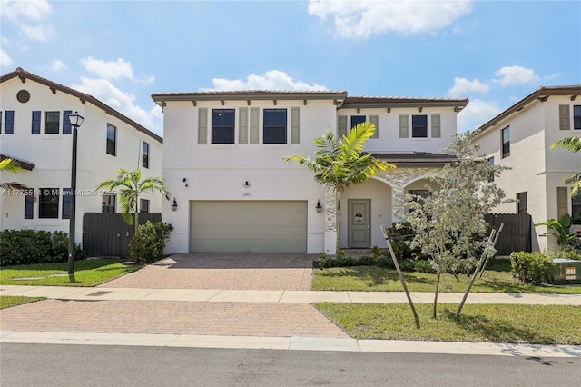 mediterranean / spanish house with fence, a tiled roof, decorative driveway, an attached garage, and stucco siding