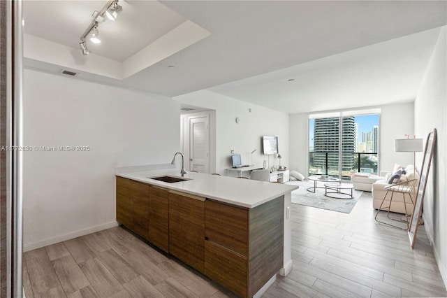 kitchen featuring a peninsula, open floor plan, brown cabinets, a sink, and light wood finished floors
