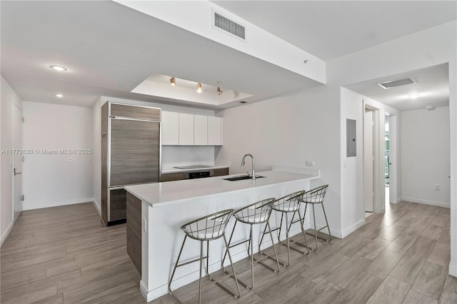 kitchen with visible vents, a peninsula, a kitchen bar, built in fridge, and a sink