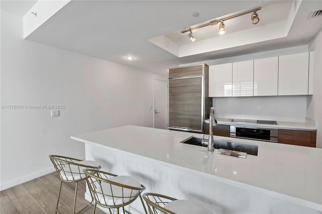 kitchen featuring oven, high end fridge, a breakfast bar area, a sink, and light wood-style flooring