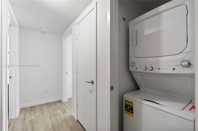 clothes washing area with baseboards, stacked washer / dryer, laundry area, and light wood-style floors