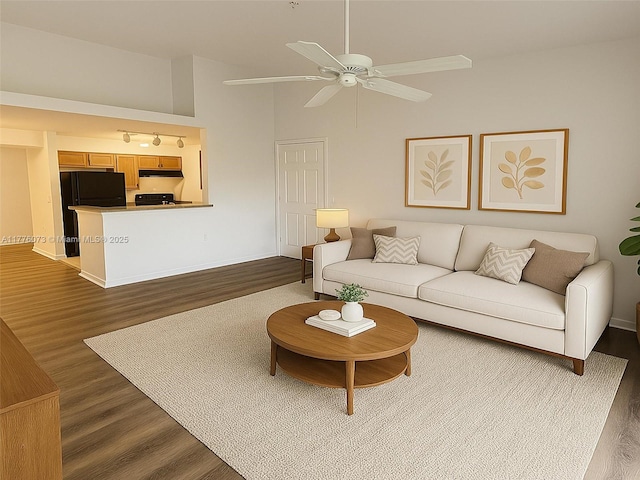 living area with a ceiling fan, dark wood-style flooring, baseboards, and a high ceiling