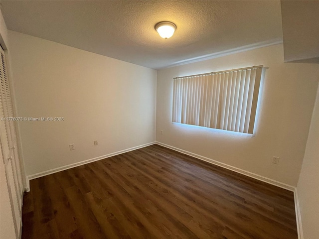 spare room with a textured ceiling, baseboards, and dark wood finished floors