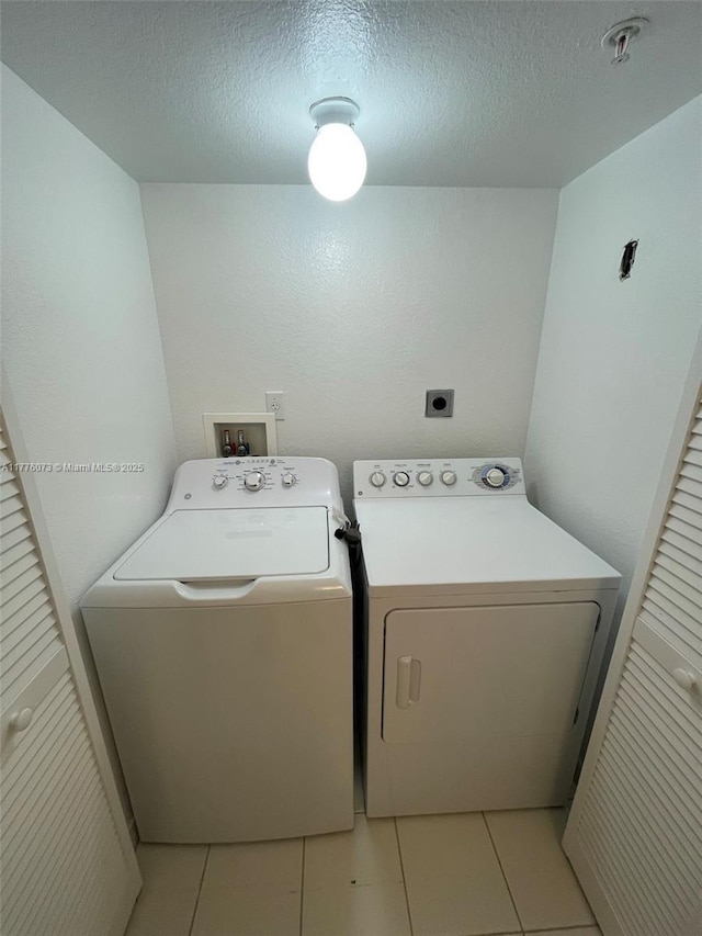 laundry area with light tile patterned floors, washer and clothes dryer, laundry area, and a textured ceiling