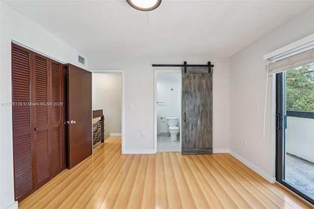 400 Valencia Ave Unit 2, Coral Gables, FL 33134 - unfurnished bedroom featuring a barn door, wood finished floors, baseboards, a closet, and ensuite bath