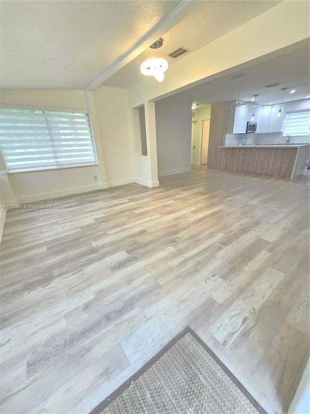 unfurnished living room featuring baseboards, visible vents, and light wood-style flooring