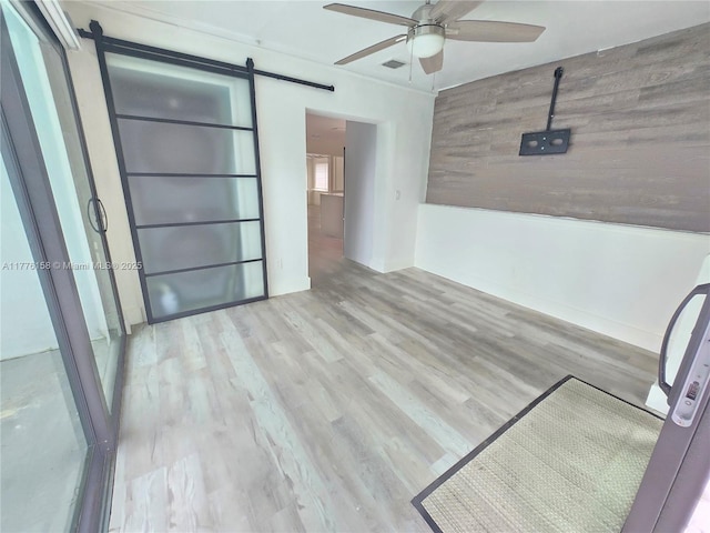 spare room featuring a barn door, ceiling fan, wood finished floors, and visible vents