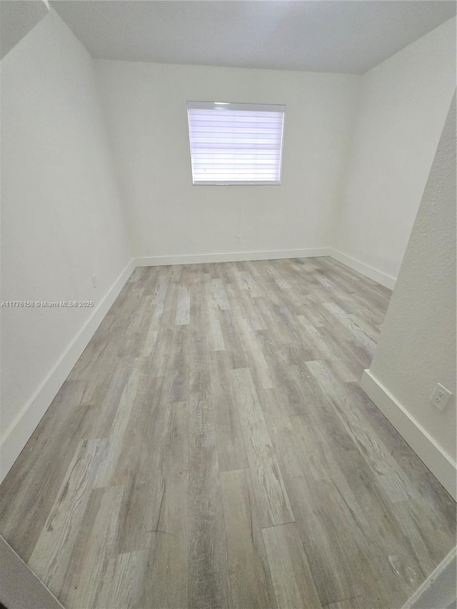 spare room with baseboards and light wood-style floors