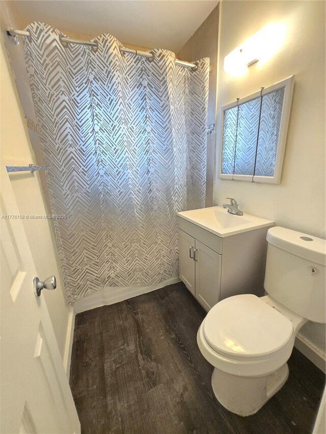 full bath with a shower with shower curtain, toilet, vanity, wood finished floors, and baseboards