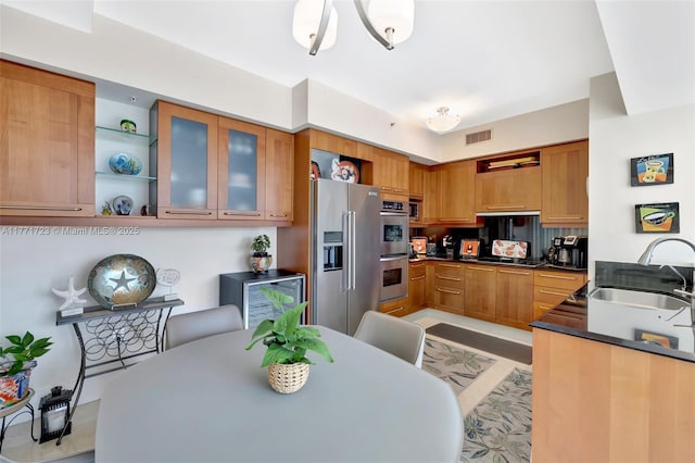 kitchen featuring a sink, glass insert cabinets, dark countertops, stainless steel appliances, and visible vents
