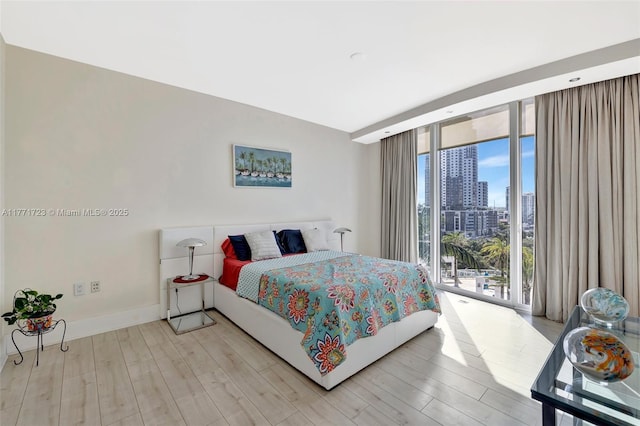 bedroom featuring a city view, access to exterior, floor to ceiling windows, light wood finished floors, and baseboards