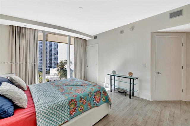 bedroom featuring wood finished floors, baseboards, expansive windows, and visible vents