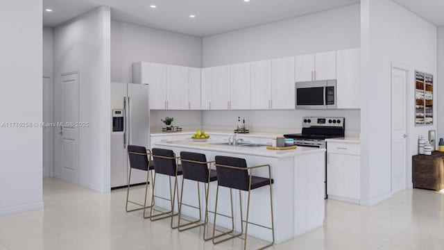 kitchen featuring an island with sink, light countertops, a kitchen breakfast bar, appliances with stainless steel finishes, and a towering ceiling