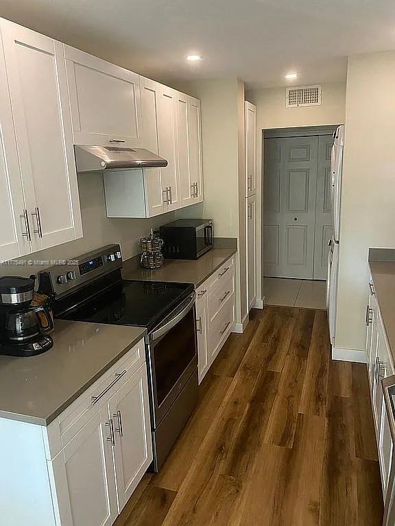 kitchen with black microwave, white cabinetry, electric range, under cabinet range hood, and visible vents