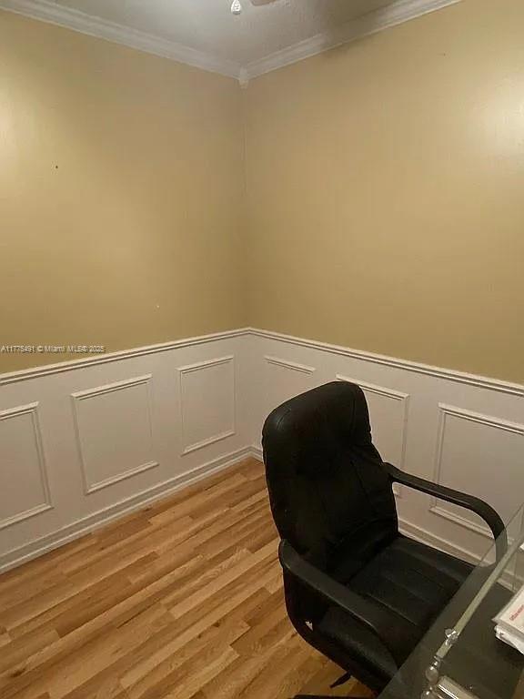 sitting room with light wood-style floors, a decorative wall, ornamental molding, and a wainscoted wall
