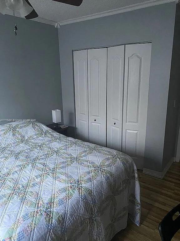 bedroom with a closet, baseboards, ornamental molding, a textured ceiling, and wood finished floors