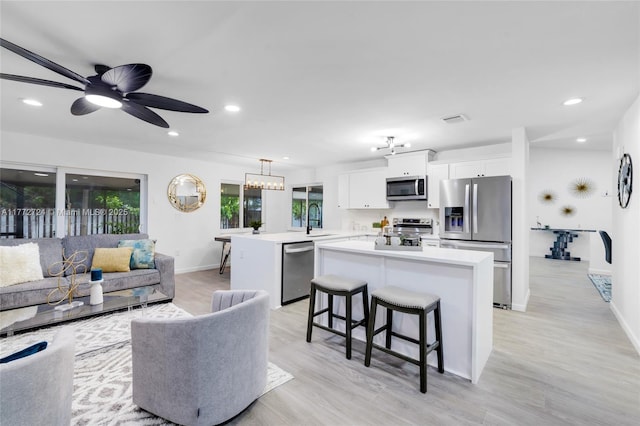 living room featuring light wood finished floors, ceiling fan with notable chandelier, baseboards, visible vents, and recessed lighting