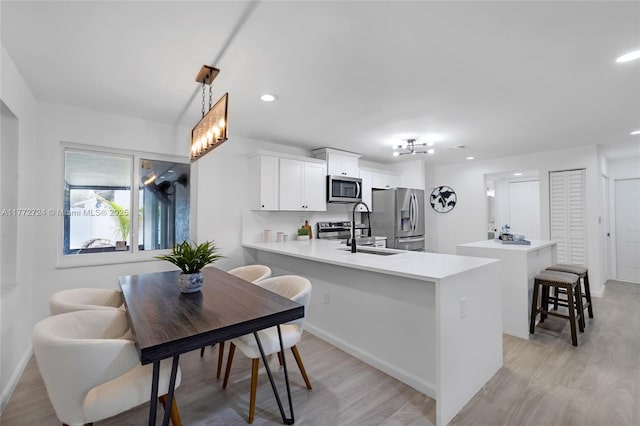 kitchen featuring a kitchen bar, a sink, light wood-style floors, a peninsula, and appliances with stainless steel finishes