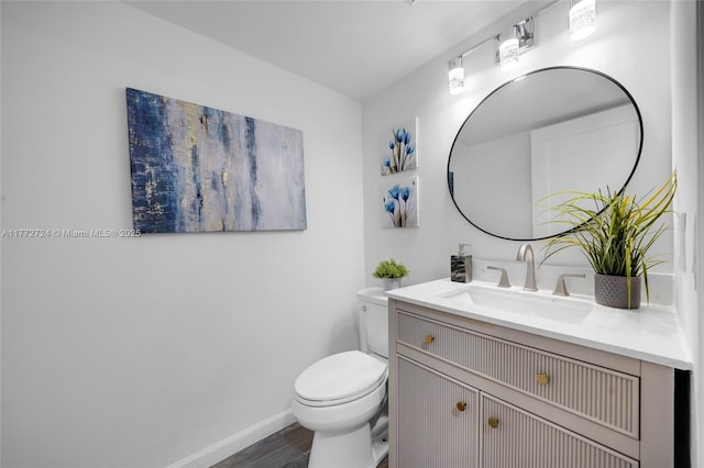 half bathroom with toilet, vanity, baseboards, and wood finished floors