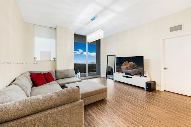 living room featuring baseboards, visible vents, wood finished floors, and a wall of windows