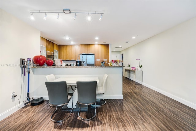 kitchen featuring baseboards, dark wood-style floors, a peninsula, appliances with stainless steel finishes, and brown cabinetry