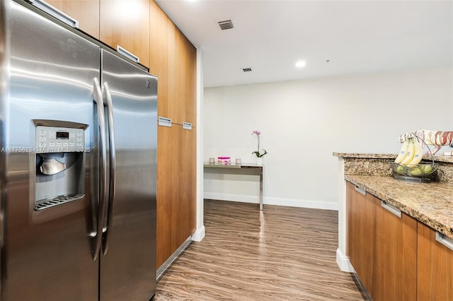 kitchen with light stone counters, stainless steel fridge, brown cabinetry, baseboards, and light wood-style floors