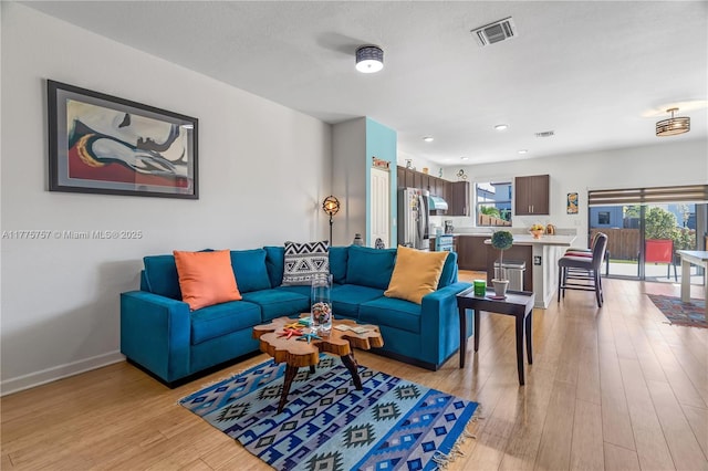 living room with baseboards, visible vents, recessed lighting, and light wood-style floors