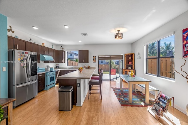 kitchen with dark brown cabinets, light wood-type flooring, a breakfast bar area, appliances with stainless steel finishes, and under cabinet range hood
