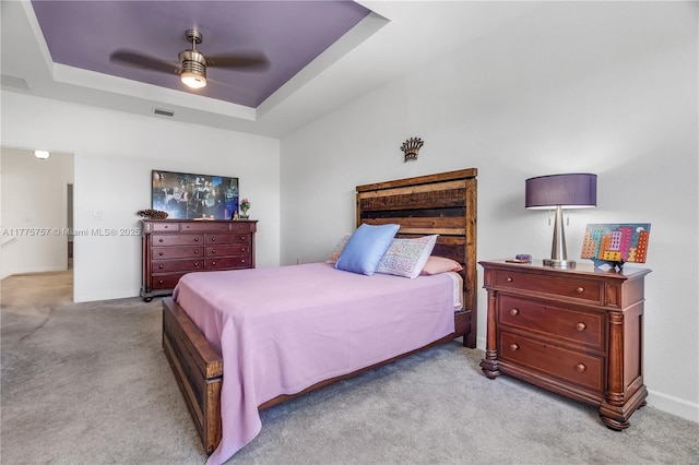 carpeted bedroom featuring a tray ceiling, visible vents, baseboards, and ceiling fan
