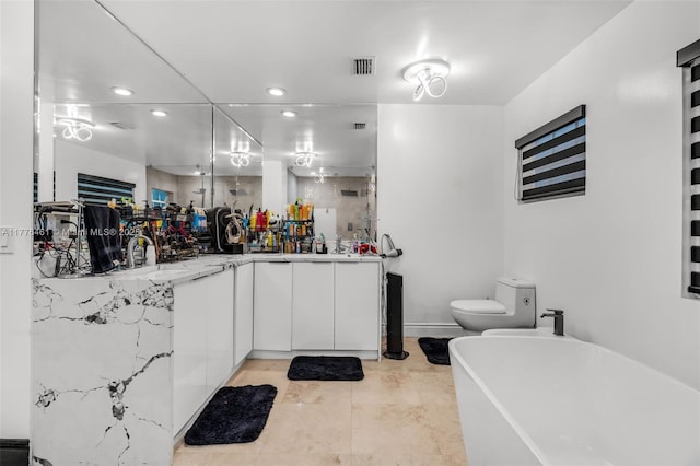 bathroom with toilet, a sink, visible vents, a freestanding bath, and double vanity