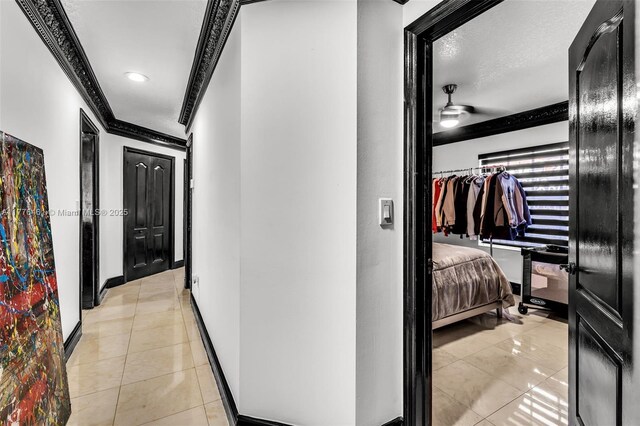 hall featuring baseboards, a textured ceiling, ornamental molding, and light tile patterned floors