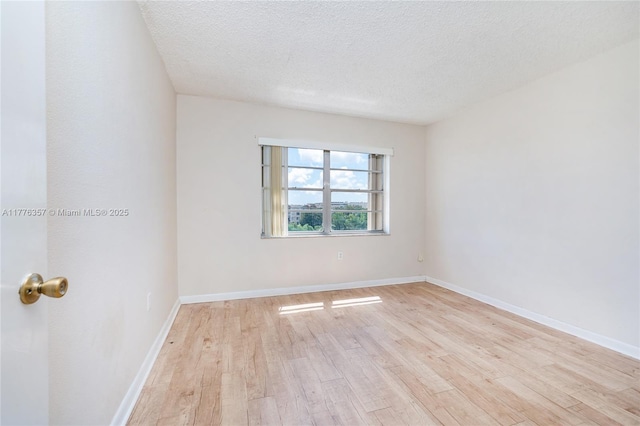 empty room featuring baseboards, a textured ceiling, and light wood-style flooring